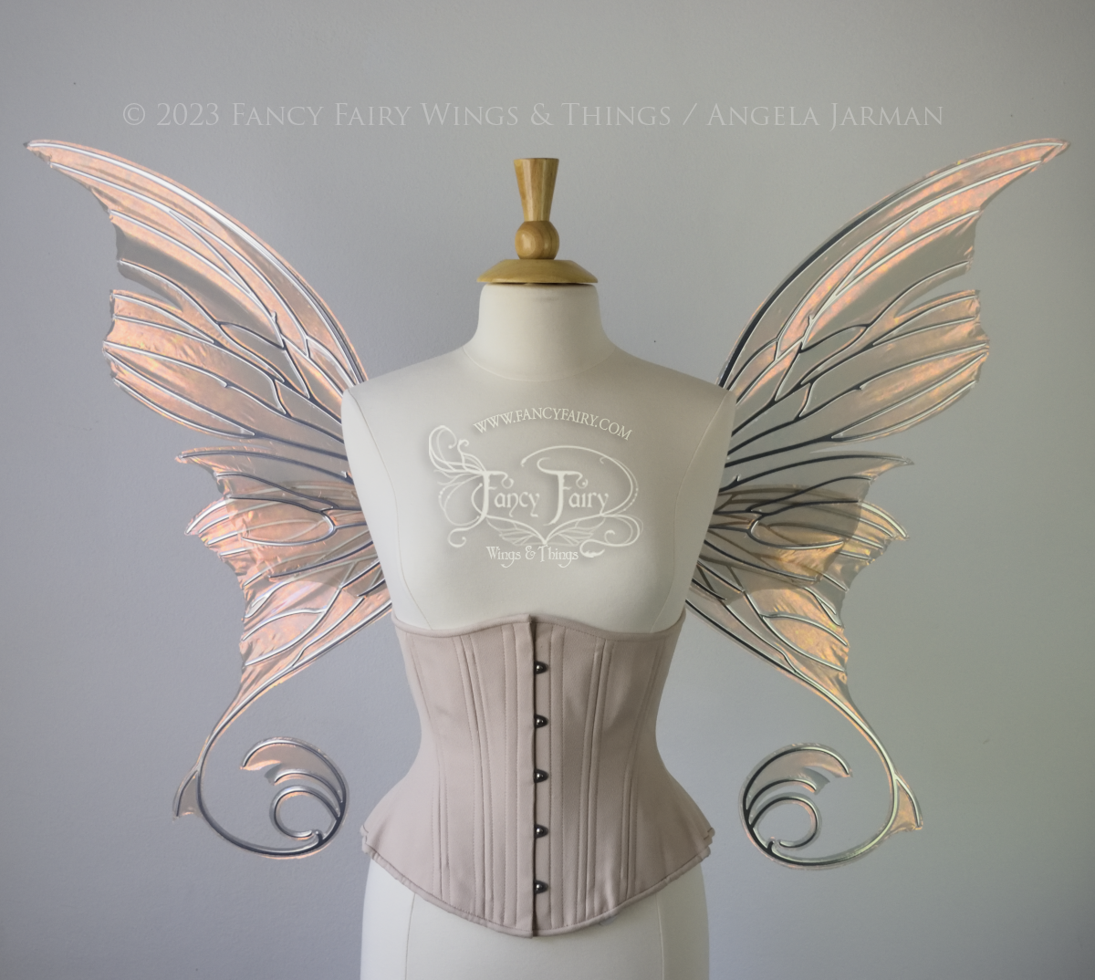 Front view of an ivory dress form wearing an alabaster underbust corset and large rose gold iridescent fairy wings with lots of intricate silver veins, some have 'thorns'. Upper panels curve slightly downwards along top edge with pointy tips, bottom panels have tails