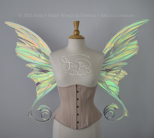 Front view of an ivory dress form wearing an alabaster underbust corset and large patina green iridescent fairy wings with lots of intricate silver veins, some have 'thorns'. Upper panels curve slightly downwards along top edge with pointy tips, bottom panels have tails