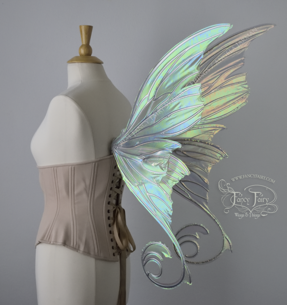 Back 3/4 view of an ivory dress form wearing an alabaster underbust corset and large rose gold iridescent fairy wings with lots of intricate silver veins, some have 'thorns'. Upper panels curve slightly downwards along top edge with pointy tips, bottom panels have tails
