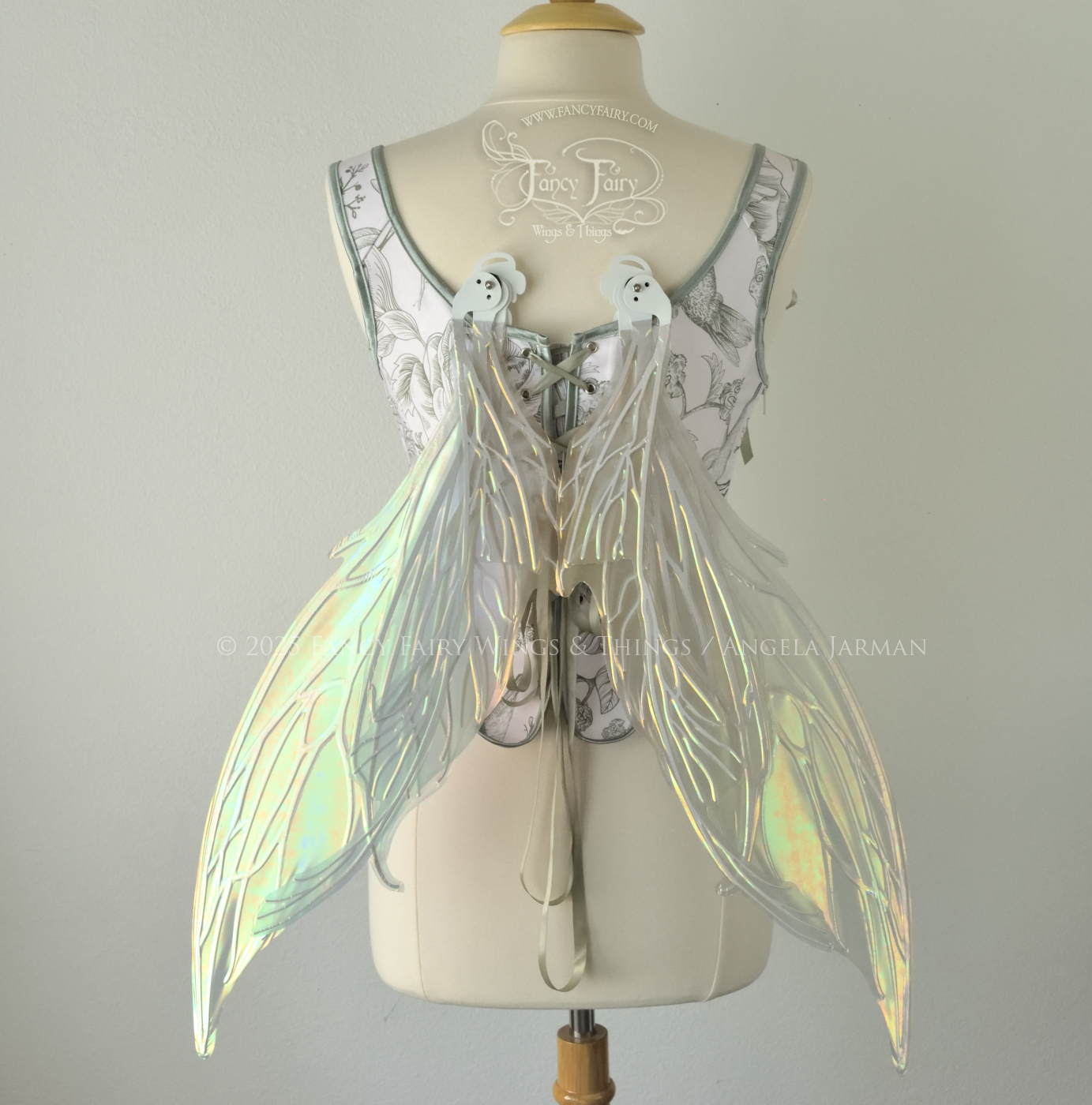 Large iridescent green fairy wings with white veins. Upper panels are elongated with pointed tips, curved ‘tail’, worn on a dress form, back view, in resting position
