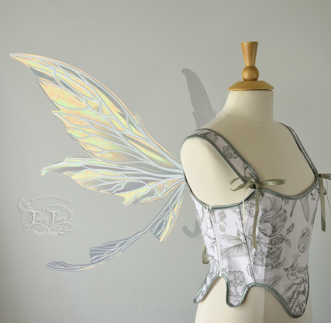 Large iridescent green fairy wings with white veins. Upper panels are elongated with pointed tips, curved ‘tail’, worn on a dress form, left side view