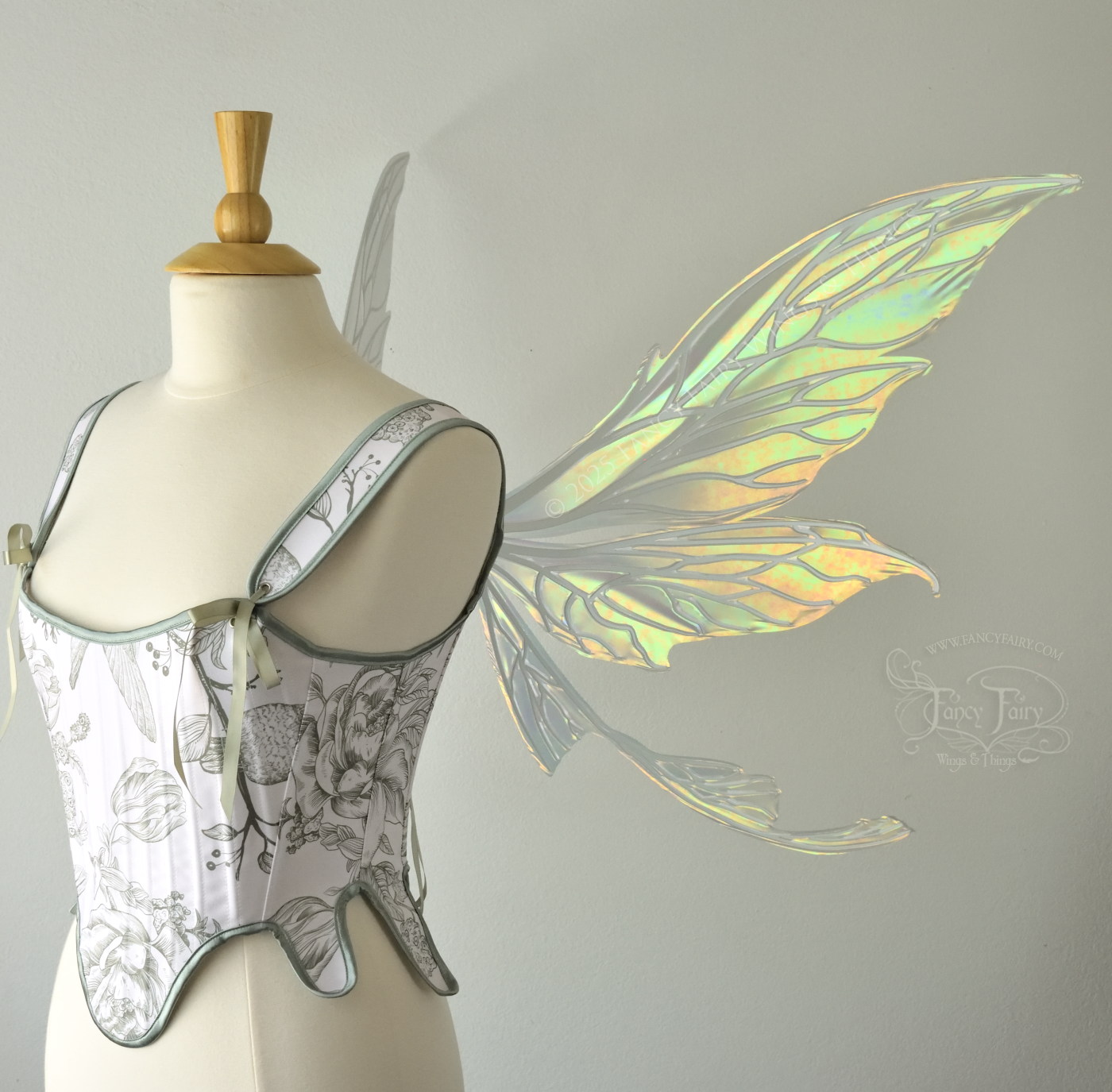 Large iridescent green fairy wings with white veins. Upper panels are elongated with pointed tips, curved ‘tail’, worn on a dress form, right side view