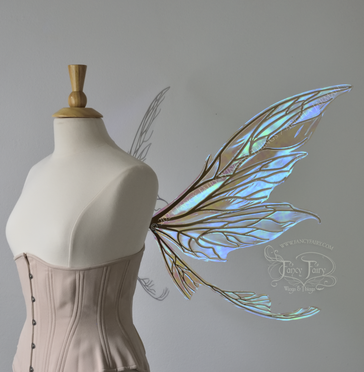 Side view of a dress form wearing an underbust corset & large blue iridescent fairy wings with gold veins. Upper panels are elongated with pointed tips, curved ‘tail’