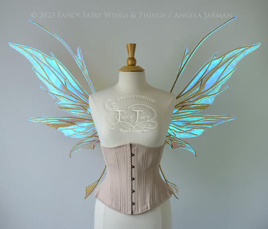 Front view of a dress form wearing an underbust corset & large blue/green iridescent fairy wings with antennae, gold veins, spikey shapes