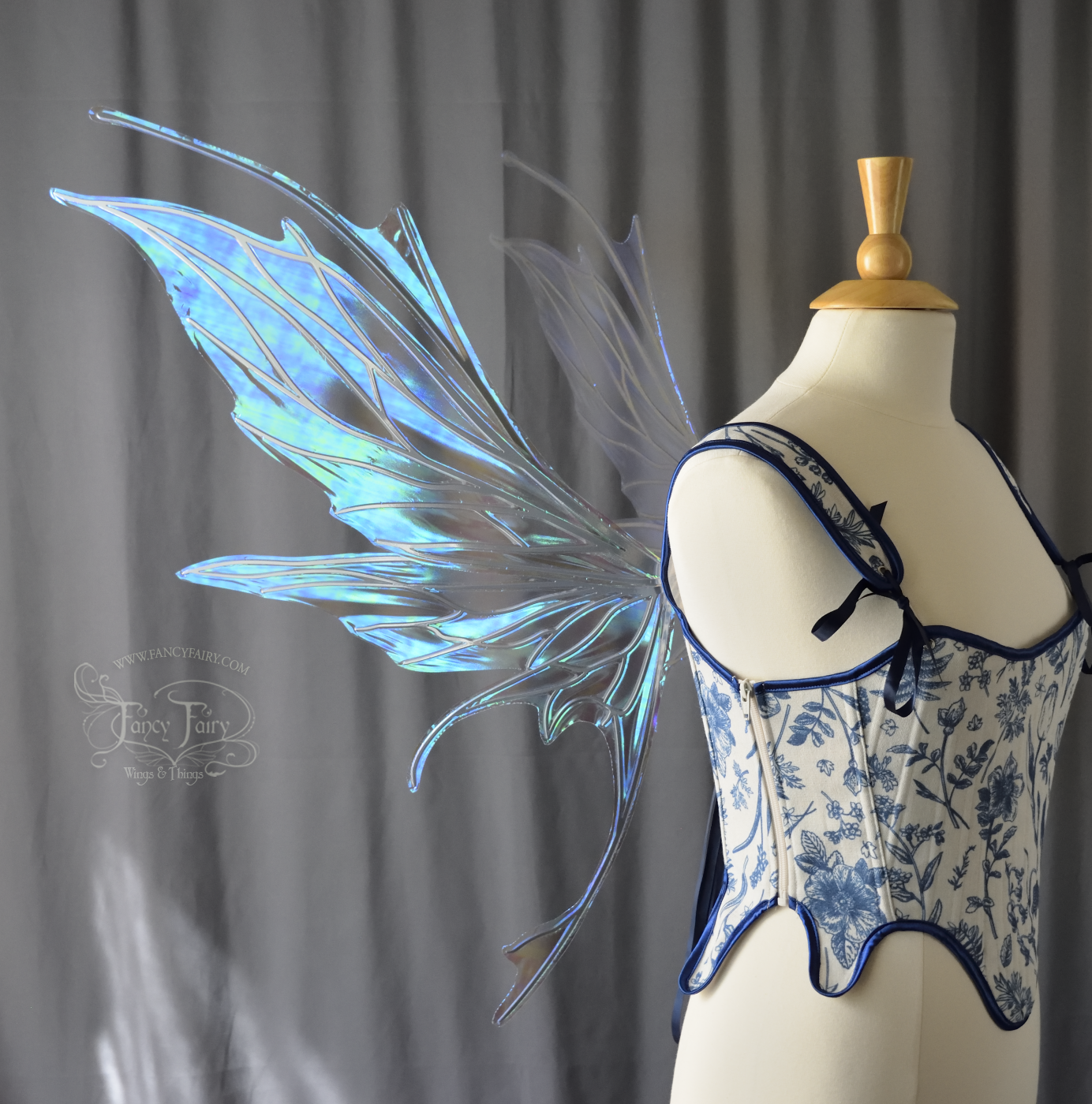 Large blue / green iridescent fairy wings with silver veins featuring antennae along the top and a spikey profile, worn on a dress form, left side view with dark grey curtain backdrop