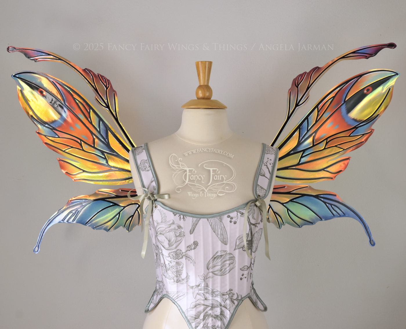 Brightly colored iridescent fairy wings in oranges, yellows, teals and blues with black veins, antennae along the top, worn on a dress form. Front view