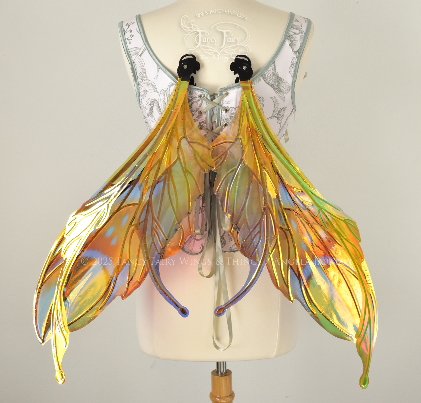 Brightly colored iridescent fairy wings in oranges, yellows, teals and blues with black veins, antennae along the top, worn on a dress form. Back view, resting position