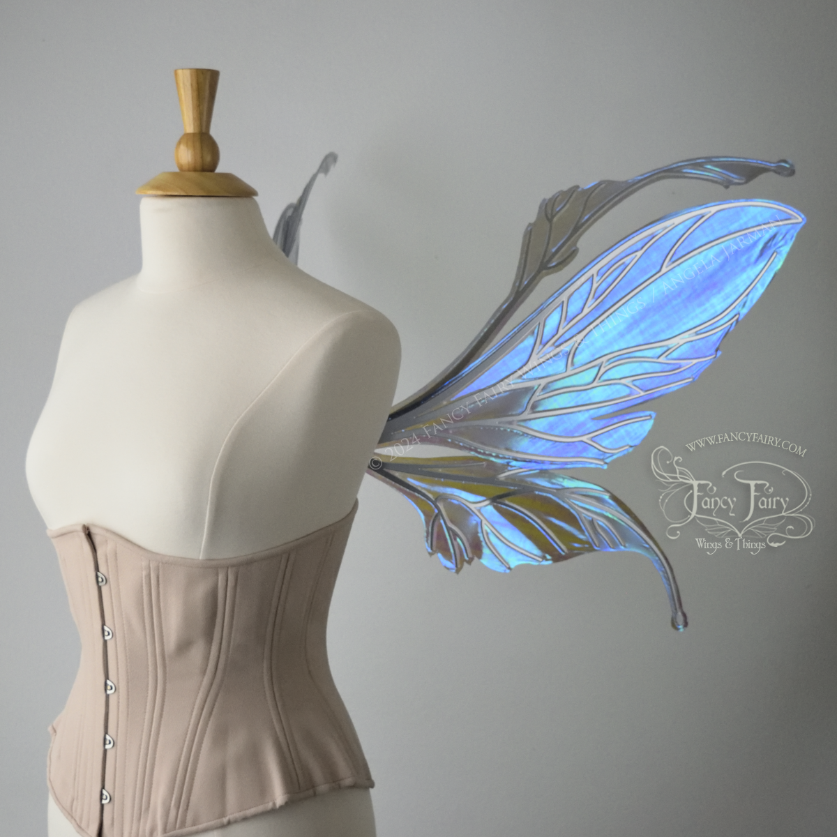 Right side view of a dress form wearing an underbust corset & large iridescent purple fairy wings with antennae. The upper panels are elongated with semi-pointed tips, the lower panels are smaller with downward curved tips, veins are silver.