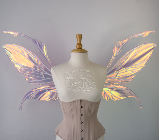 Front view of an ivory dress form wearing an alabaster underbust corset and large fairy wings featuring antennae along the top. The upper panels are elongated with semi-pointed tips, the lower panels are smaller with slender tips that curve downward. They are pink iridescent with a orange & yellow shine and the veins are white. The background is plain white and my logo and copyright notice are visible. 