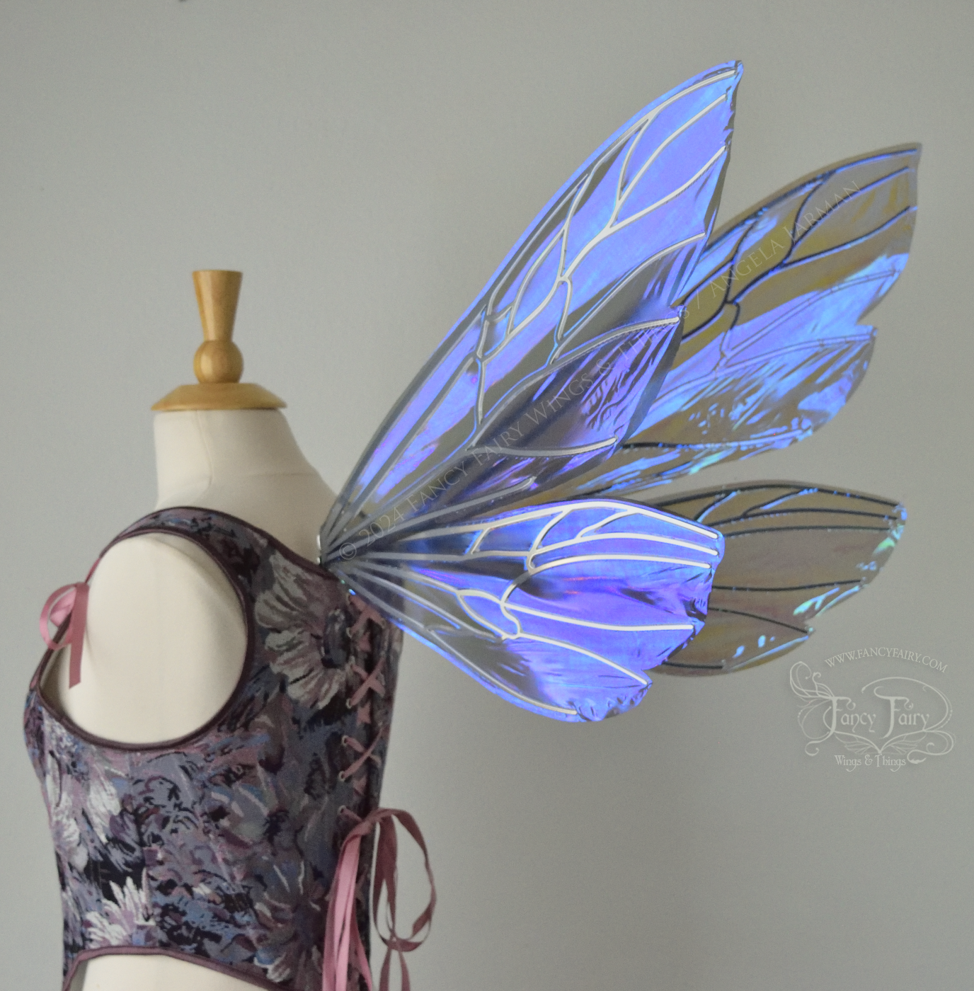 Large fairy wings similar in shape to wasp wings, are iridescent violet / blue with silver veins, back 3/4 view