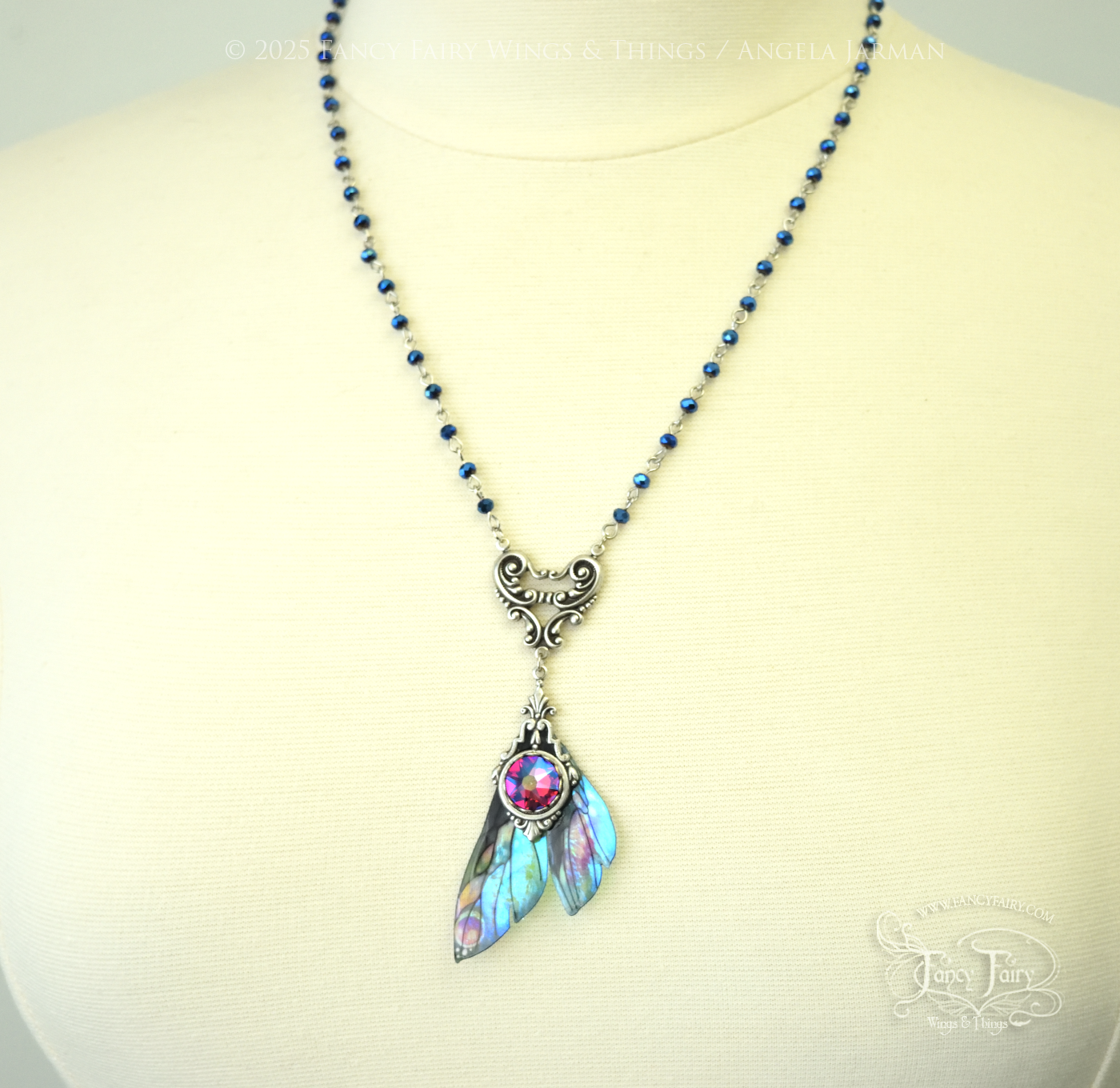 Iridescent fairy wing pendant necklace in teals with pink accents and silver filigree, hanging from a silver chain with blue faceted beads, worn on a dress form