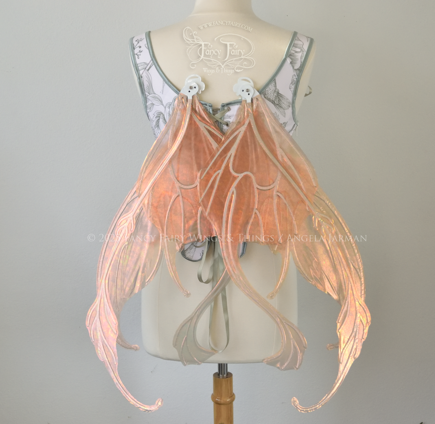 Rose gold iridescent transparent fairy wings with antennae and tails on the bottom panels with white veins, worn on a dress form, back view, in resting position