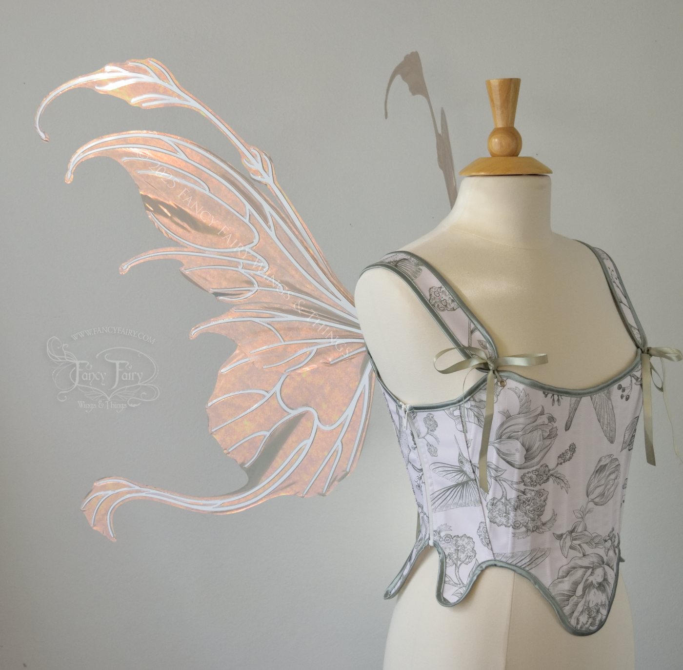 Rose gold iridescent transparent fairy wings with antennae and tails on the bottom panels with white veins, worn on a dress form, left side view