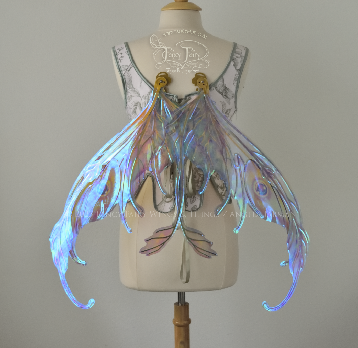 Iridescent pastel rainbow fairy wings with downward curved tips, antennae and appendages, with gold veins, worn on a dress form, back view, in resting position