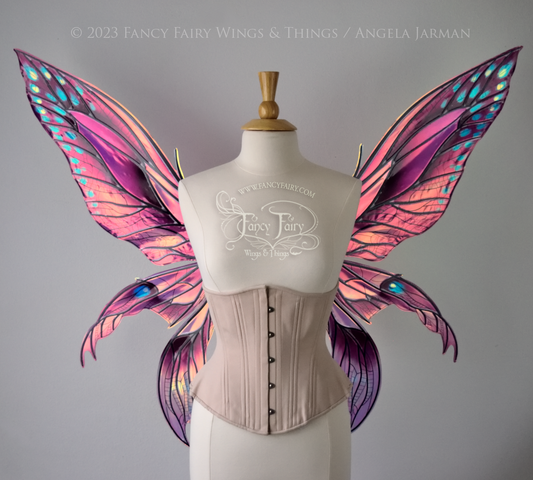 Front view of an ivory dress form wearing an alabaster underbust corset and large multicolor iridescent fairy wings. Upper panels are elongated with pointed tips, 2 lower panels curve downward, lots of thin vein detail