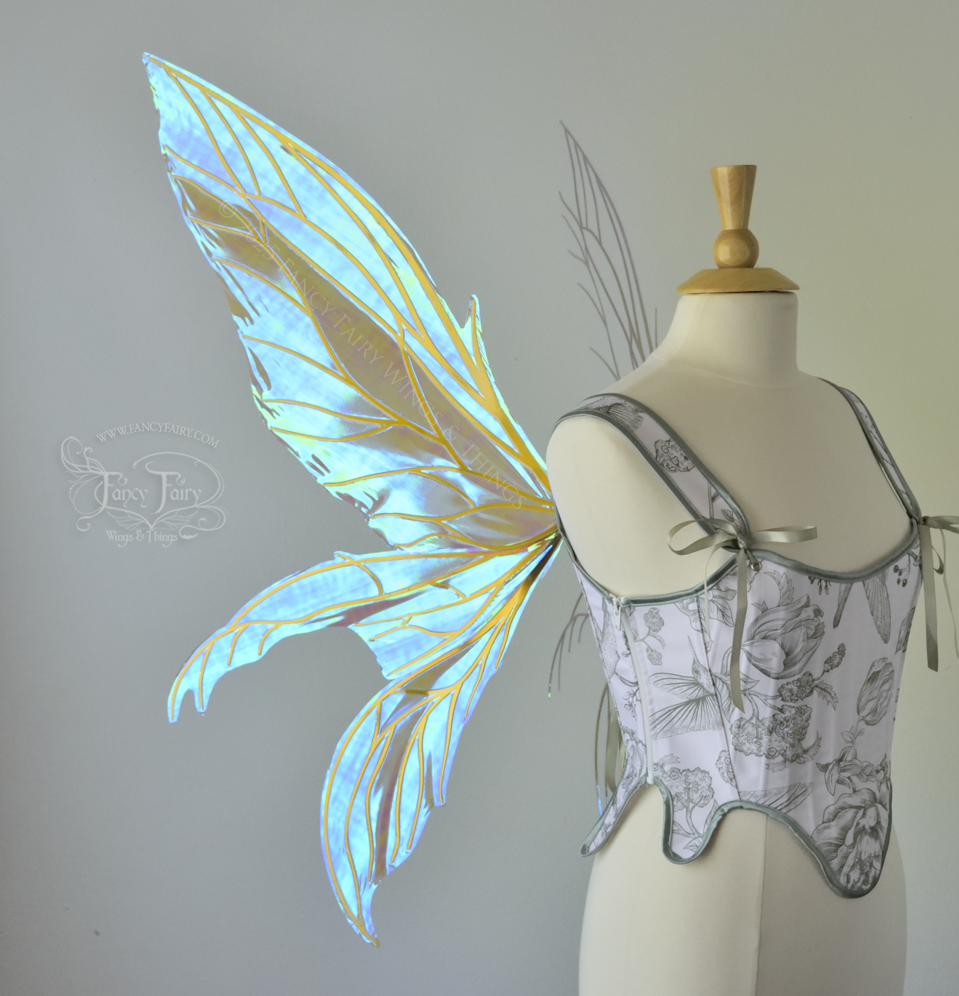 Large transparent blue/green dragonfly-like iridescent fairy wings with gold veins have 3 elongated panels on each side, worn on a dress form, left side view