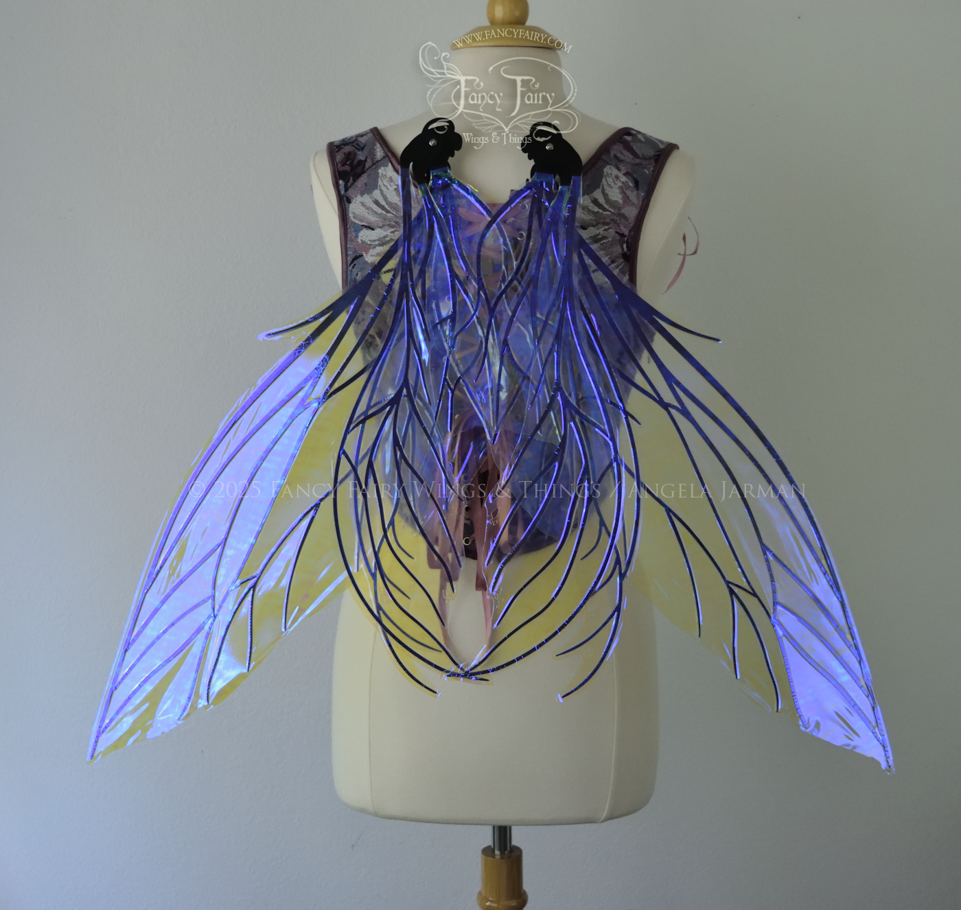 Large violet dragonfly-like iridescent fairy wings with black veins have 3 elongated panels on each side, worn on a dress form, back view in resting position