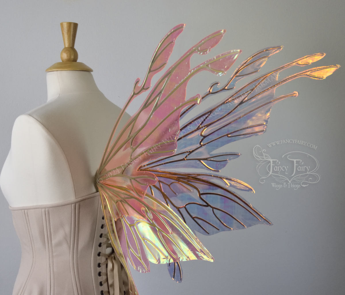 Back 3/4 view of an ivory dress form wearing an alabaster underbust corset & large pink & orange iridescent fairy wings with elongated upper panels with petal like appendages at the tips & antennae, the veins are gold