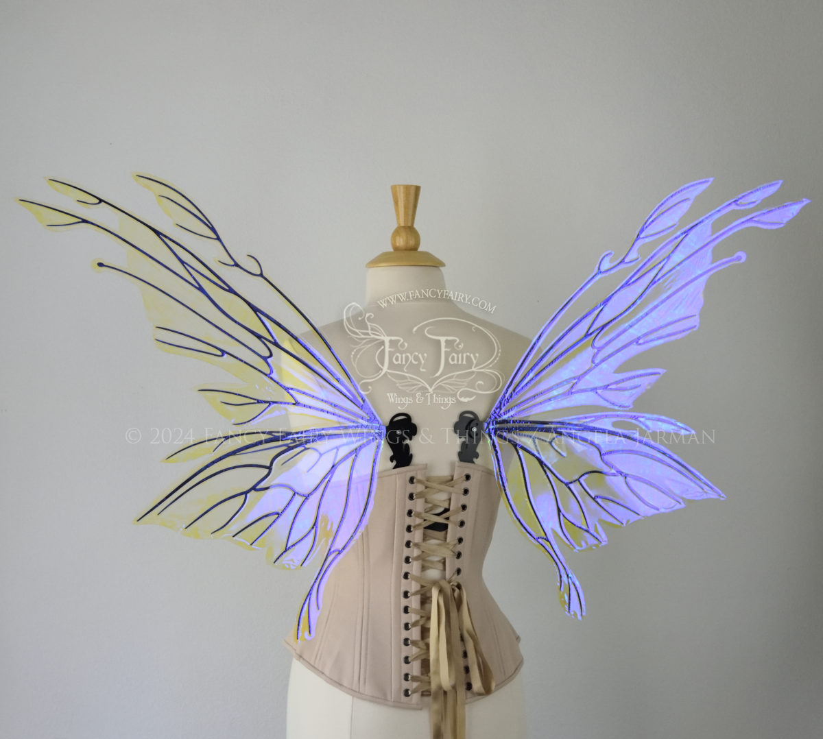 Back view of an ivory dress form wearing an alabaster underbust corset & large violet iridescent fairy wings with elongated upper panels with petal like appendages at the tips & antennae, the veins are black
