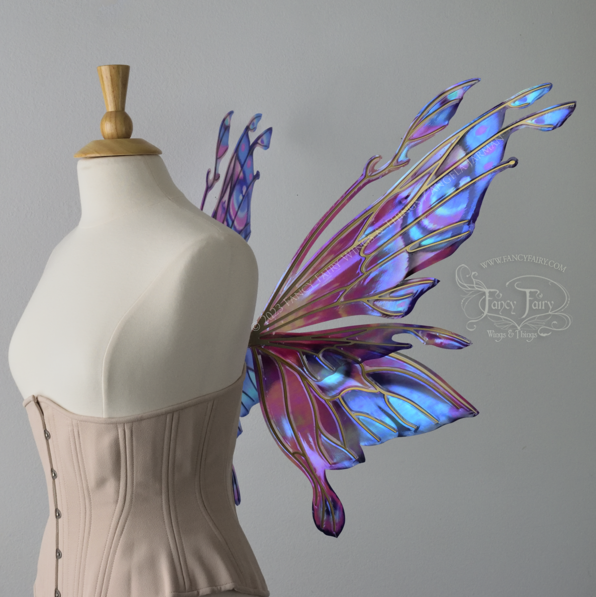 Right side view of an ivory dress form wearing an underbust corset & 'Goblin Princess' magenta & blue painted iridescent wings w/ gold veins
