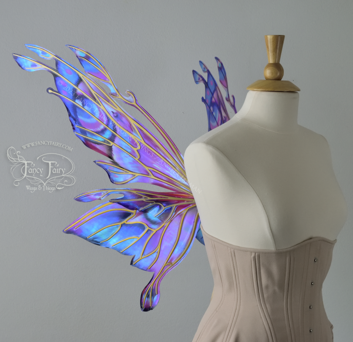 Left side view of an ivory dress form wearing an underbust corset & 'Goblin Princess' magenta & blue painted iridescent wings w/ gold veins