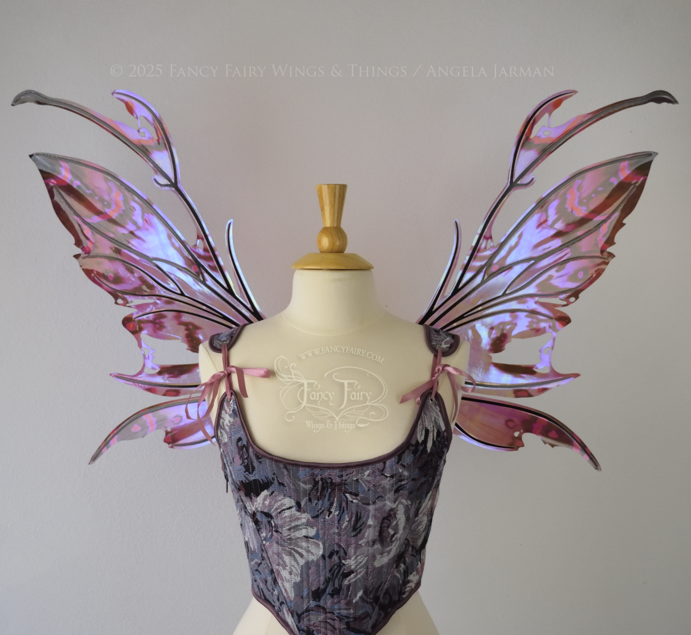 Iridescent fairy wings in mauve, violet, red & black with spikey antennae & tattered edges with holes is worn on a dress form which is also wearing violet & pink floral patterned stays / bodice