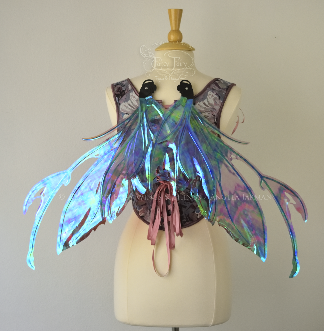 Iridescent fairy wings in mauve, violet, red & black with spikey antennae & tattered edges with holes is worn on a dress form which is also wearing violet & pink floral patterned stays / bodice, back view, in resting position