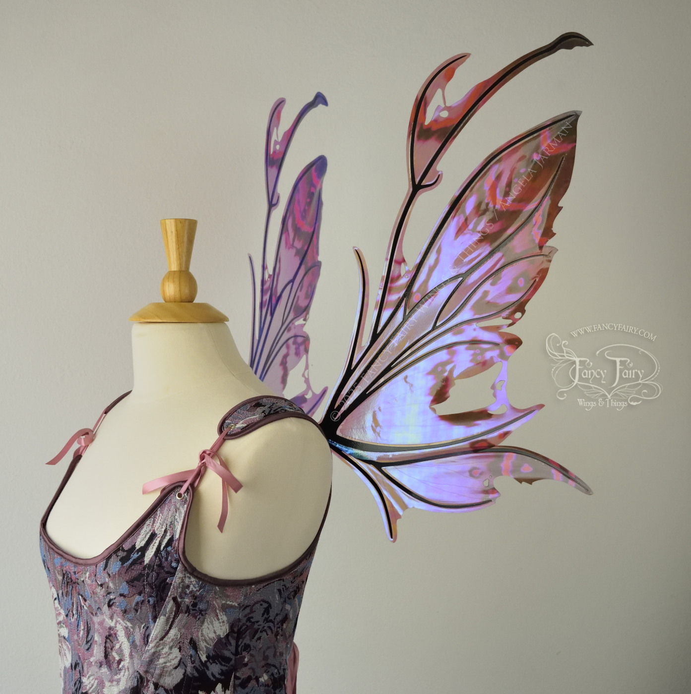 Iridescent fairy wings in mauve, violet, red & black with spikey antennae & tattered edges with holes is worn on a dress form which is also wearing violet & pink floral patterned stays / bodice, right side view