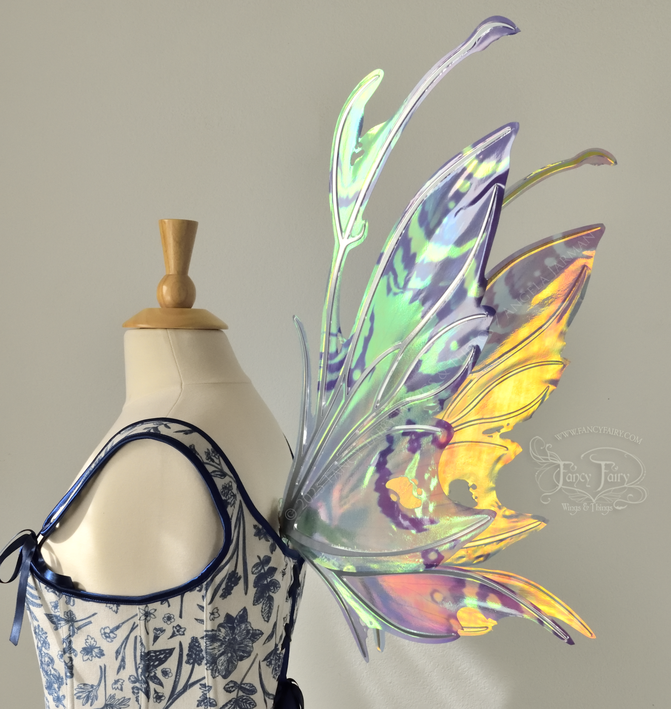 Teal, blue and silver iridescent fairy wings with a spikey profile and antennae are viewed from side /back, with the back of the background wing shining with gold and orange, worn on a dress form