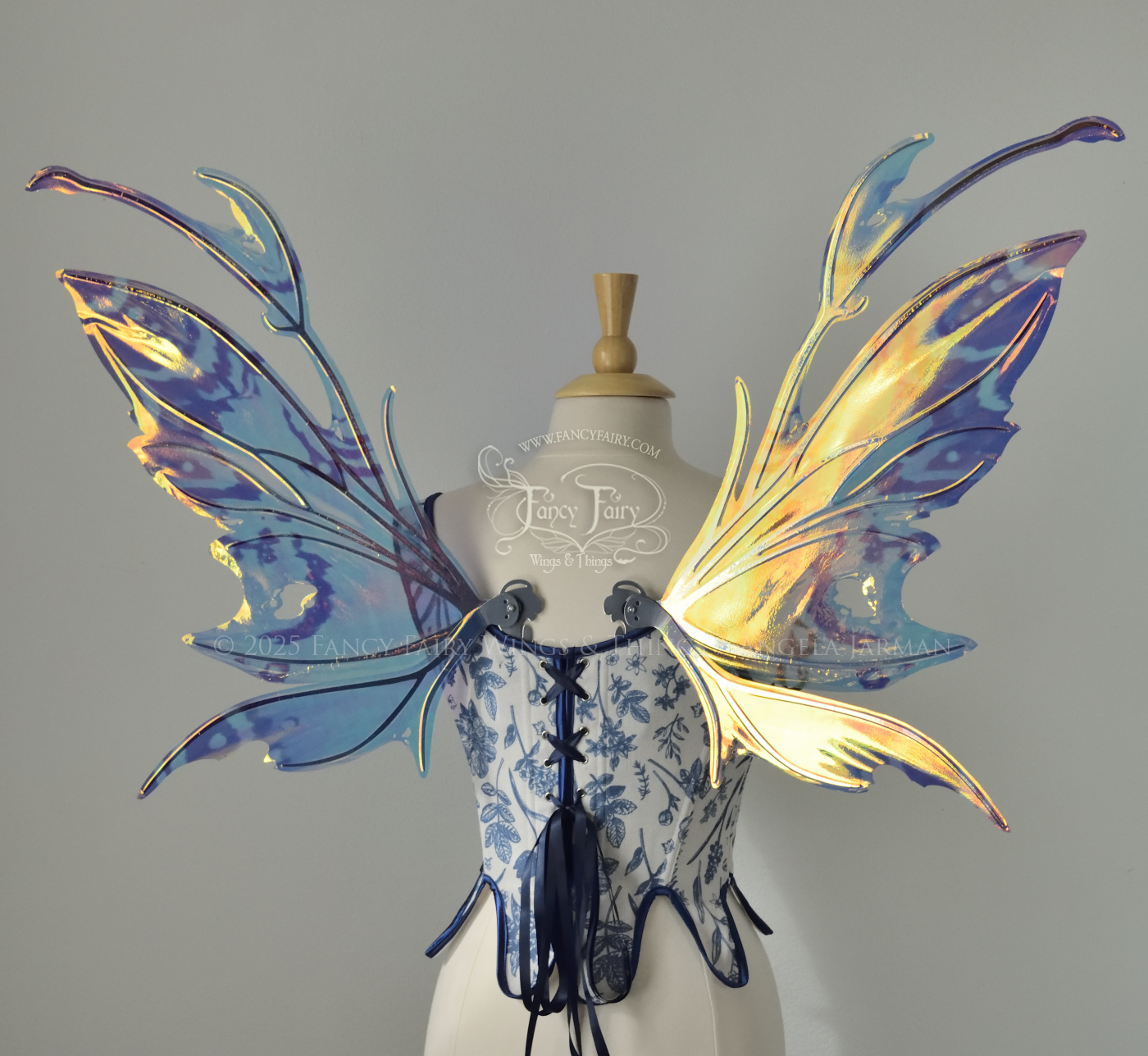 Teal, blue and silver iridescent fairy wings with a spikey profile and antennae are viewed from the back, worn on a dress form