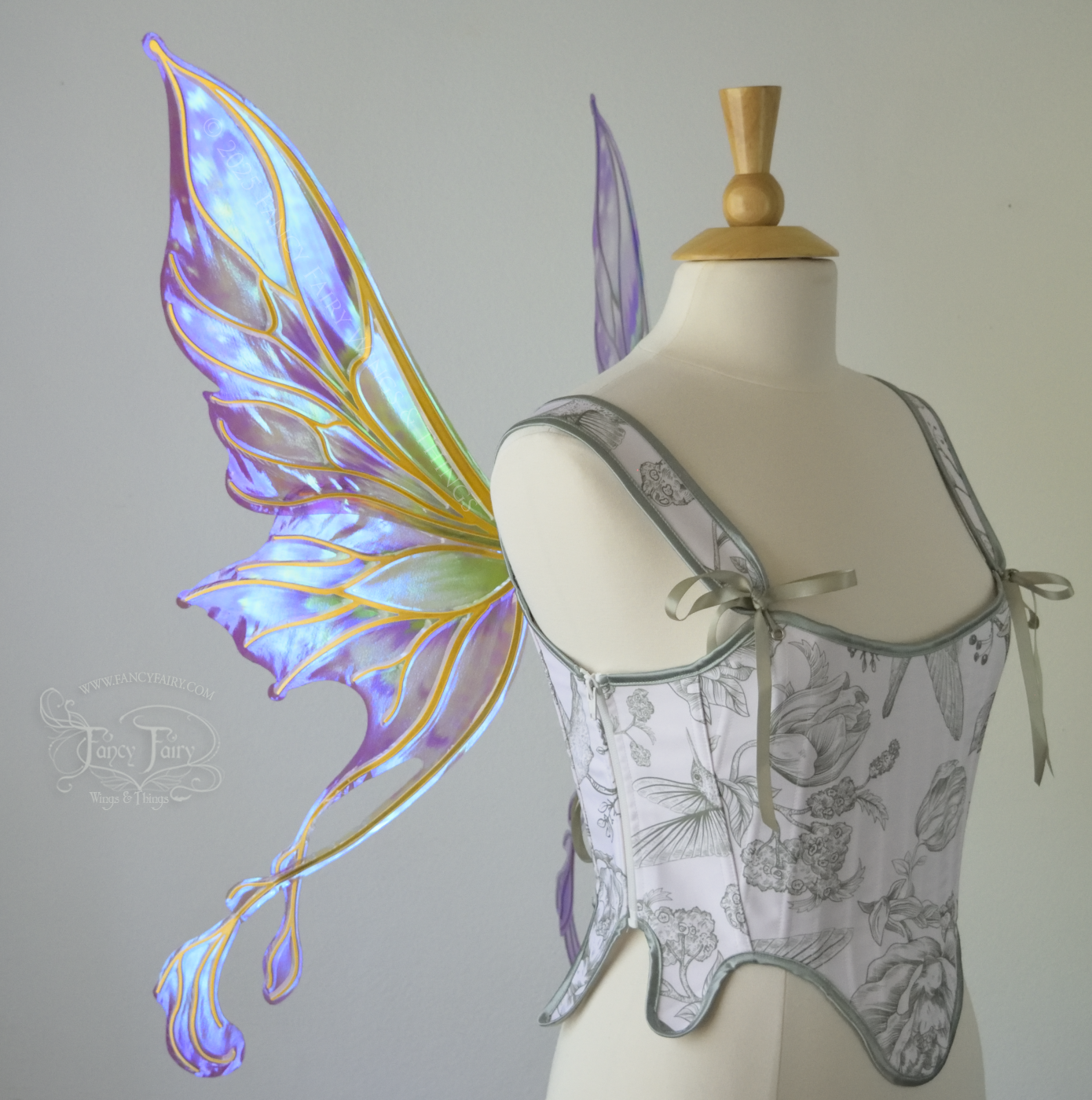 Iridescent & transparent purple & green fairy wings with gold veins and 2 swirling tails, worn on a dress form, left side view