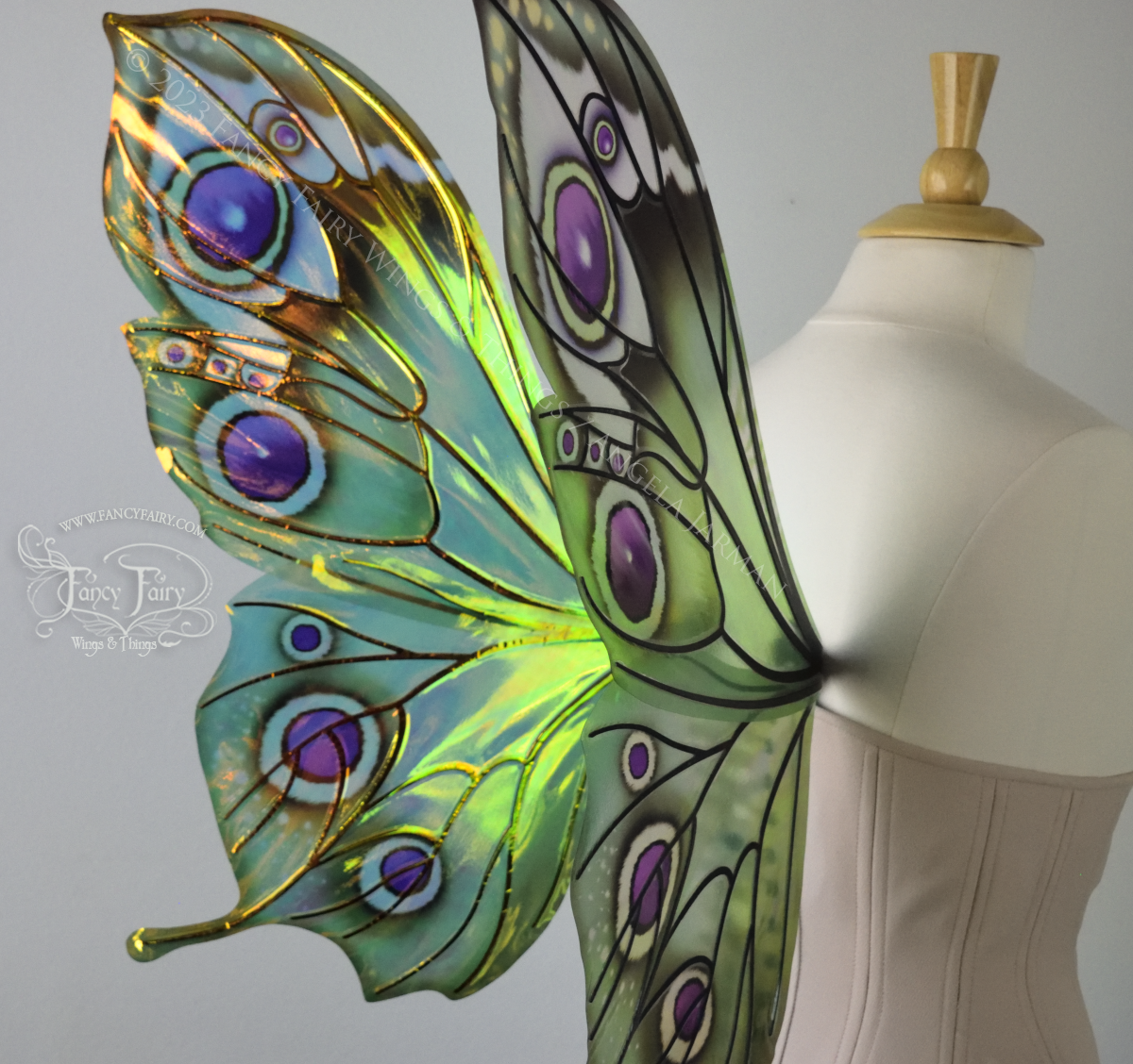 Back left 3/4 closeup view of iridescent green, black and fuchsia costume fairy wings, worn on a dressform