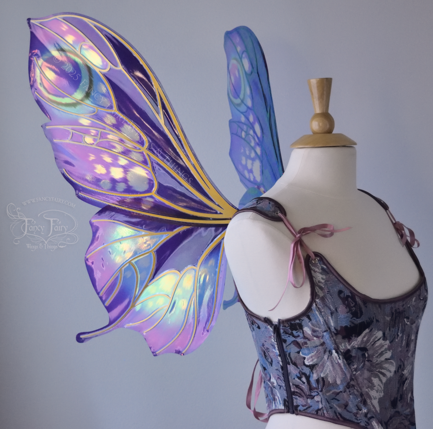 Large butterfly-esque iridescent fairy wings in shades of plum purple, blue and pink with art nouveau style gold veins, worn on a dress form, left side view