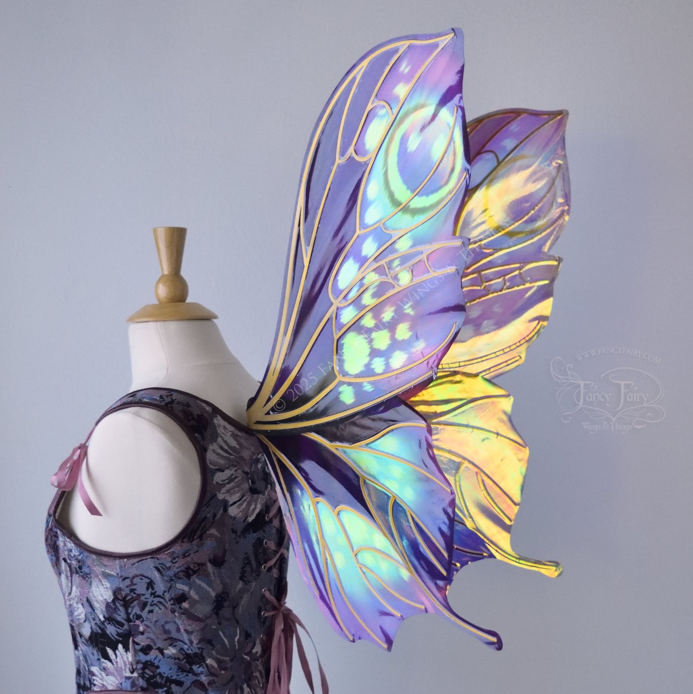Large butterfly-esque iridescent fairy wings in shades of plum purple, blue and pink with art nouveau style gold veins, worn on a dress form, back 3/4 view