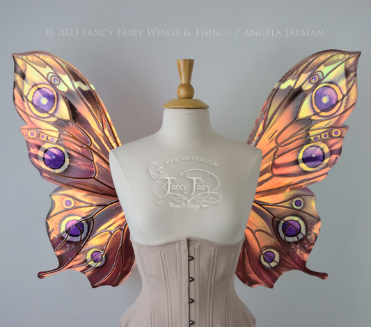 Front view of iridescent butterfly-shaped fairy wings painted with warm autumn colors & purple and black 'eye' spots, worn on a dress form