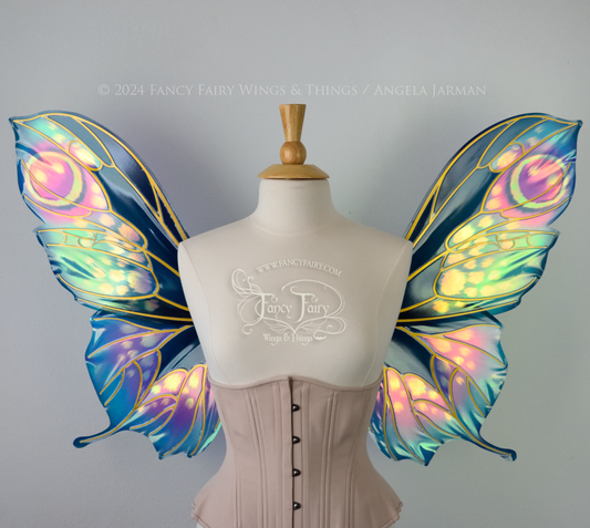 Front view of butterfly shaped iridescent wings in shades of teal with pink and lavender accents with gold veins, worn on a dressform
