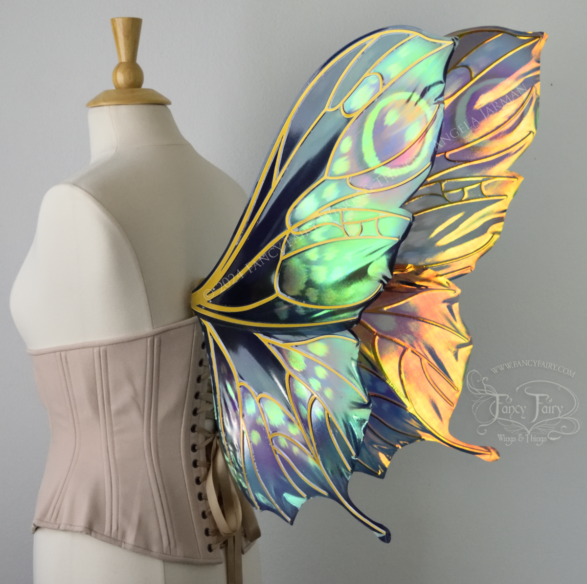 Back 3/4 view of butterfly shaped iridescent wings in shades of teal with pink and lavender accents with gold veins, worn on a dressform