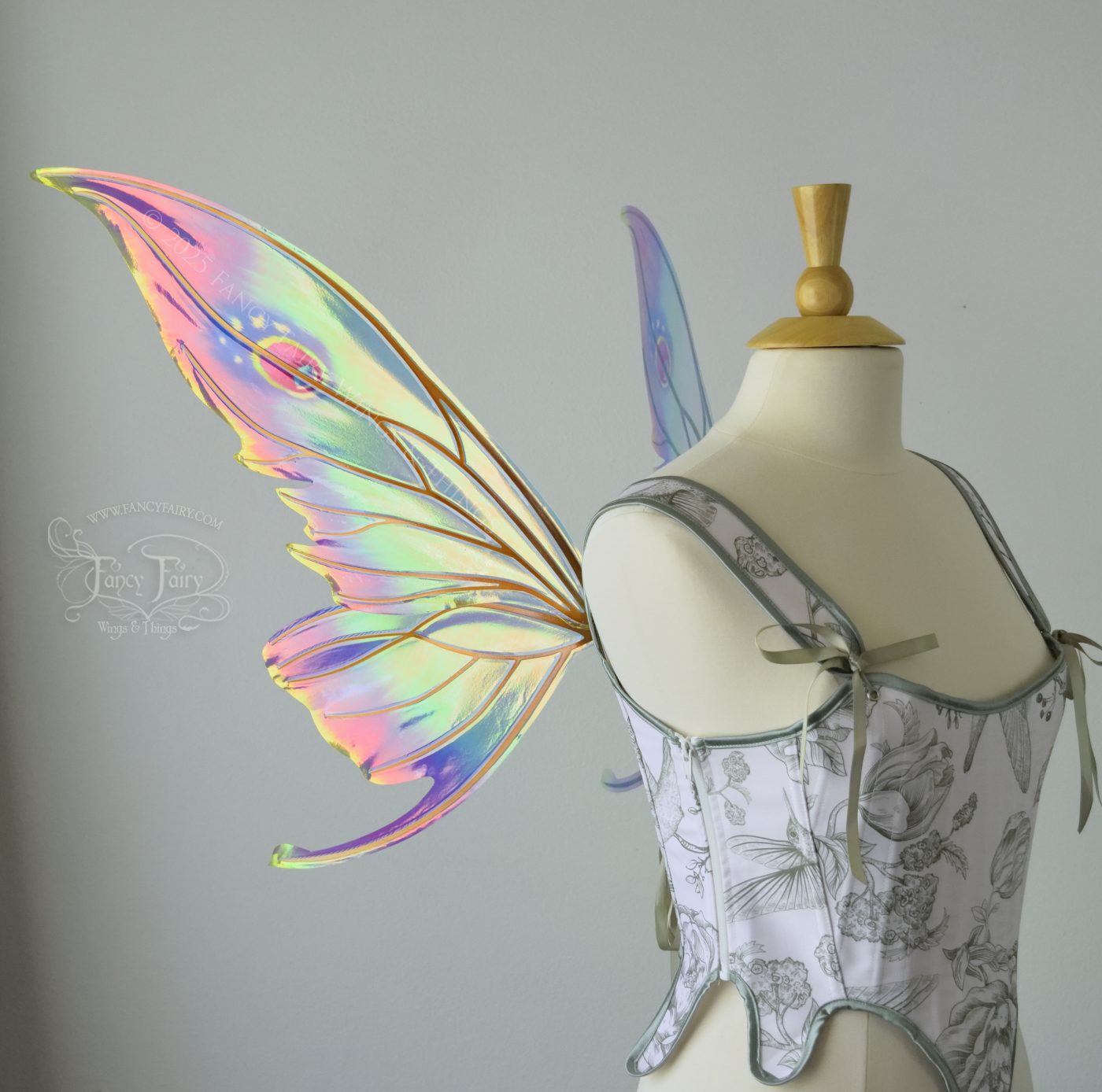 Iridescent rainbow fairy wings with elongated slightly downward curved tips on upper panels, and small tail that swoops up from bottom panels, worn on a dress form, left side view