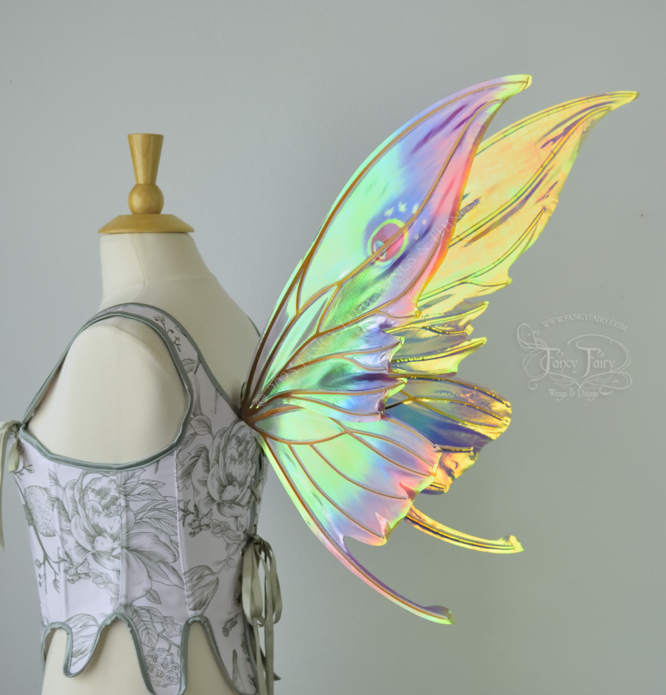 Iridescent rainbow fairy wings with elongated slightly downward curved tips on upper panels, and small tail that swoops up from bottom panels, worn on a dress form, back right 3/4 side view