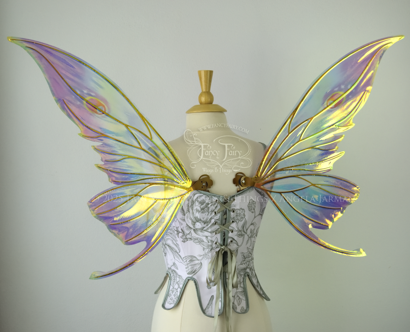 Iridescent rainbow fairy wings with elongated slightly downward curved tips on upper panels, and small tail that swoops up from bottom panels, worn on a dress form, back view