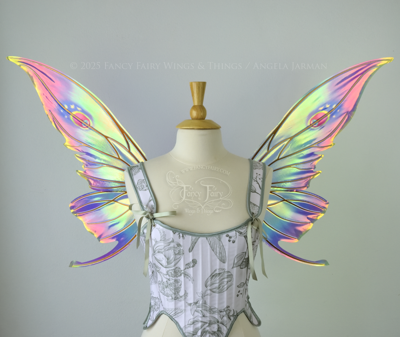 Iridescent rainbow fairy wings with elongated slightly downward curved tips on upper panels, and small tail that swoops up from bottom panels, worn on a dress form, front view