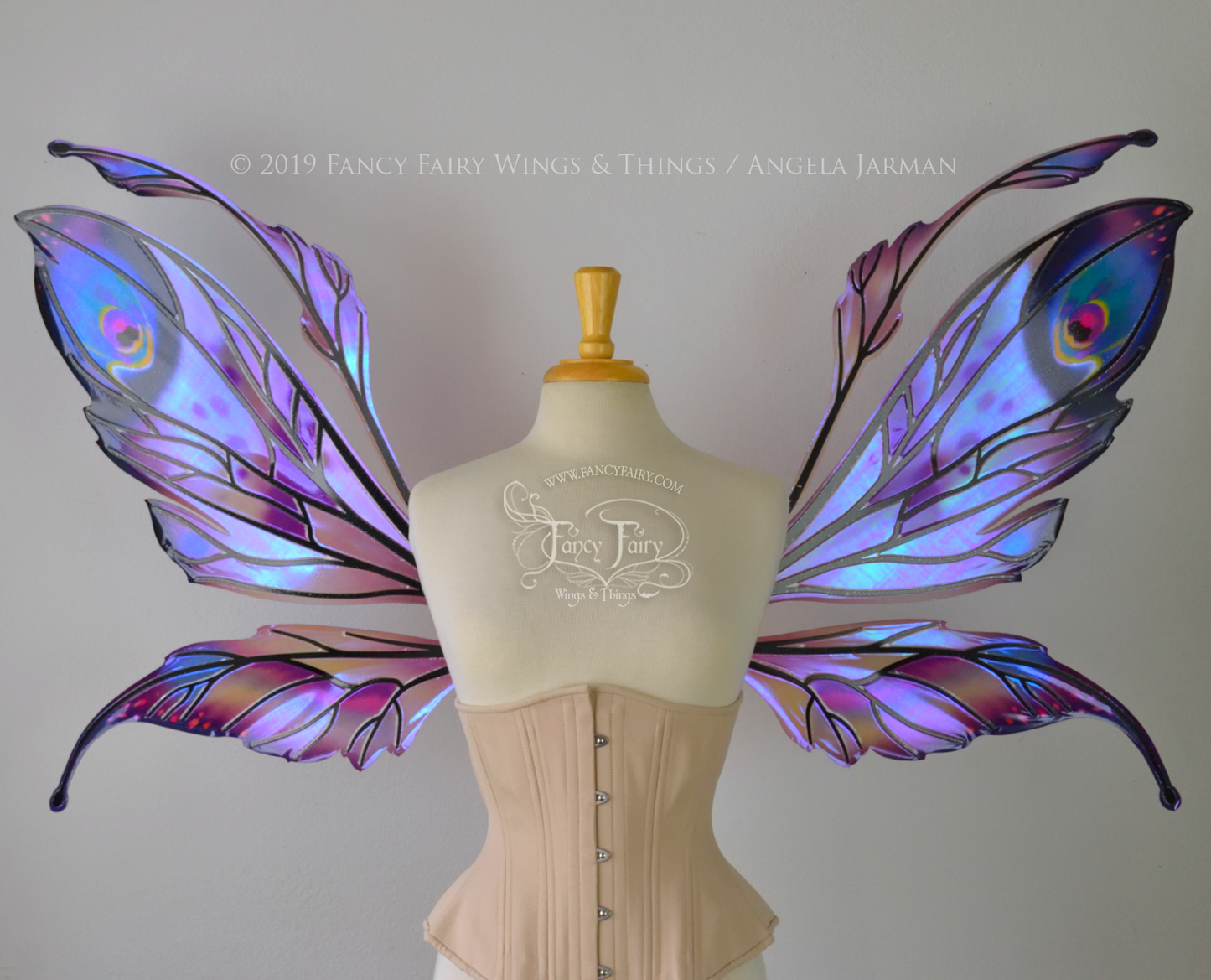 Front view of a dress form wearing an underbust corset & extra large iridescent fairy wings with mauve purple & blue color pattern