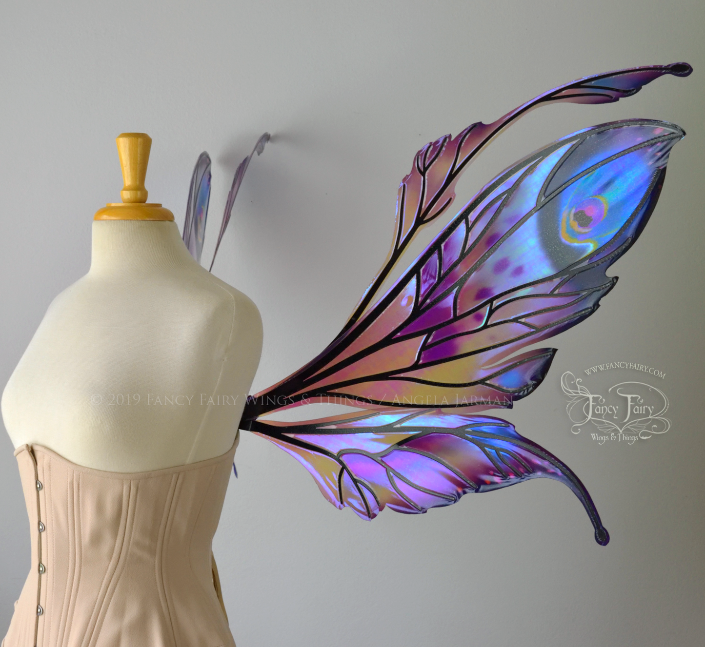 Right side view of a dress form wearing an underbust corset & extra large iridescent fairy wings with mauve purple & blue color pattern