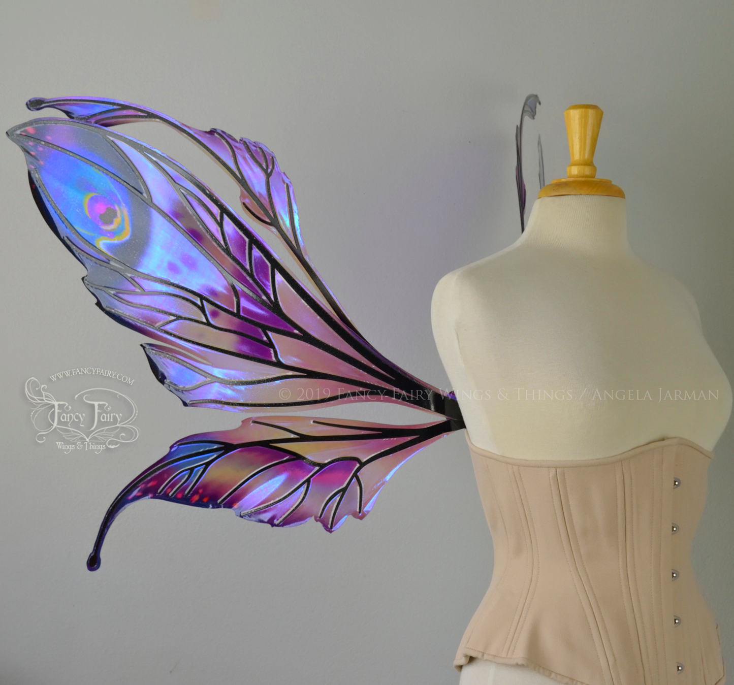Left side view of a dress form wearing an underbust corset & extra large iridescent fairy wings with mauve purple & blue color pattern