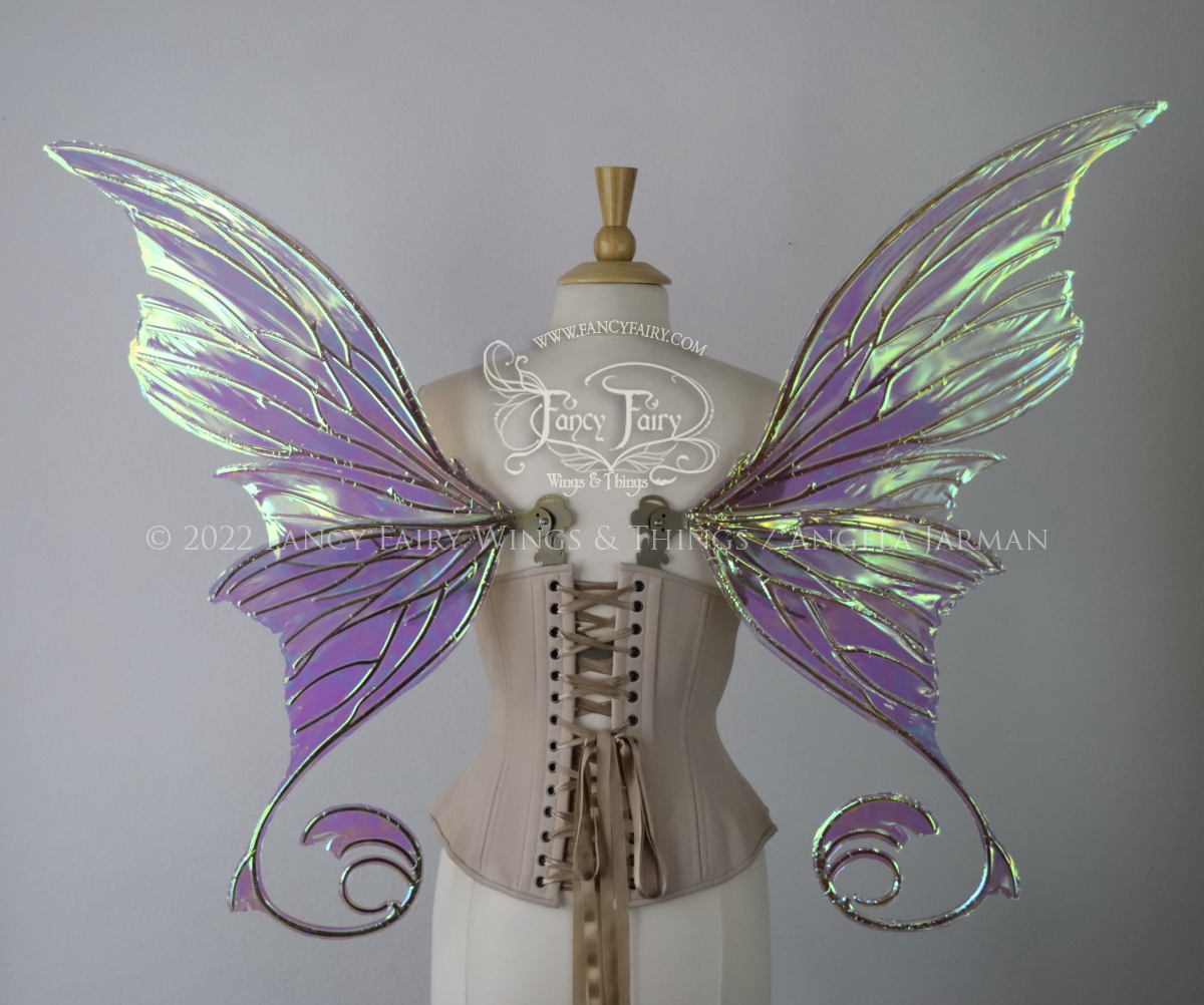Back view of a dress form wearing an underbust corset & large green iridescent fairy wings with lots of intricate gold veins, some have 'thorns'. Upper panels curve slightly downwards along top edge with pointy tips, bottom panels have tails
