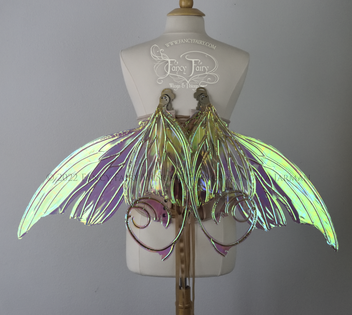 Back view of a dress form wearing an underbust corset & large green iridescent fairy wings in resting position with lots of intricate gold veins, some have 'thorns'. Upper panels curve slightly downwards along top edge with pointy tips, bottom panels have tails