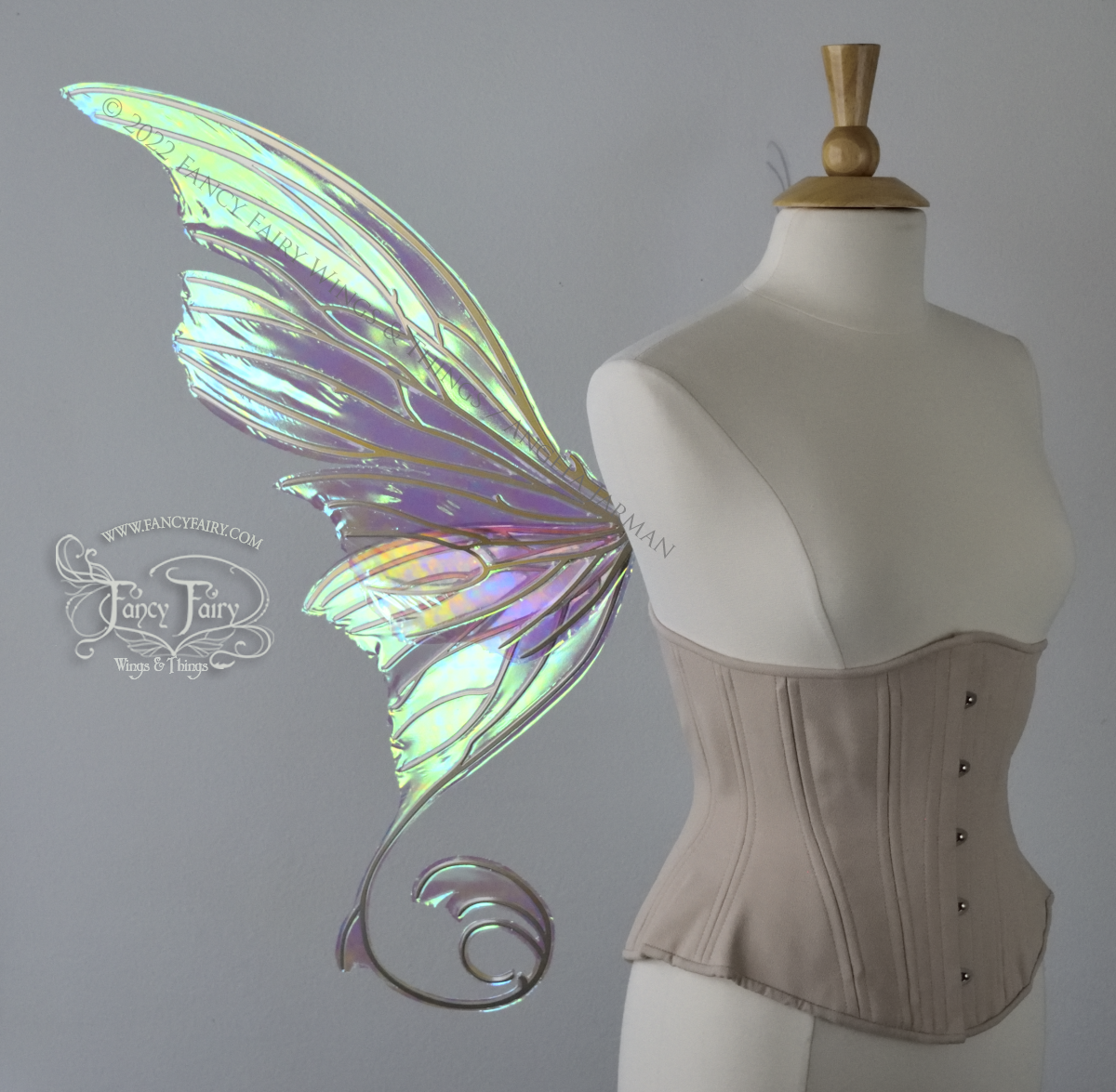 Left side view of a dress form wearing an underbust corset & large green iridescent fairy wings with lots of intricate gold veins, some have 'thorns'. Upper panels curve slightly downwards along top edge with pointy tips, bottom panels have tails