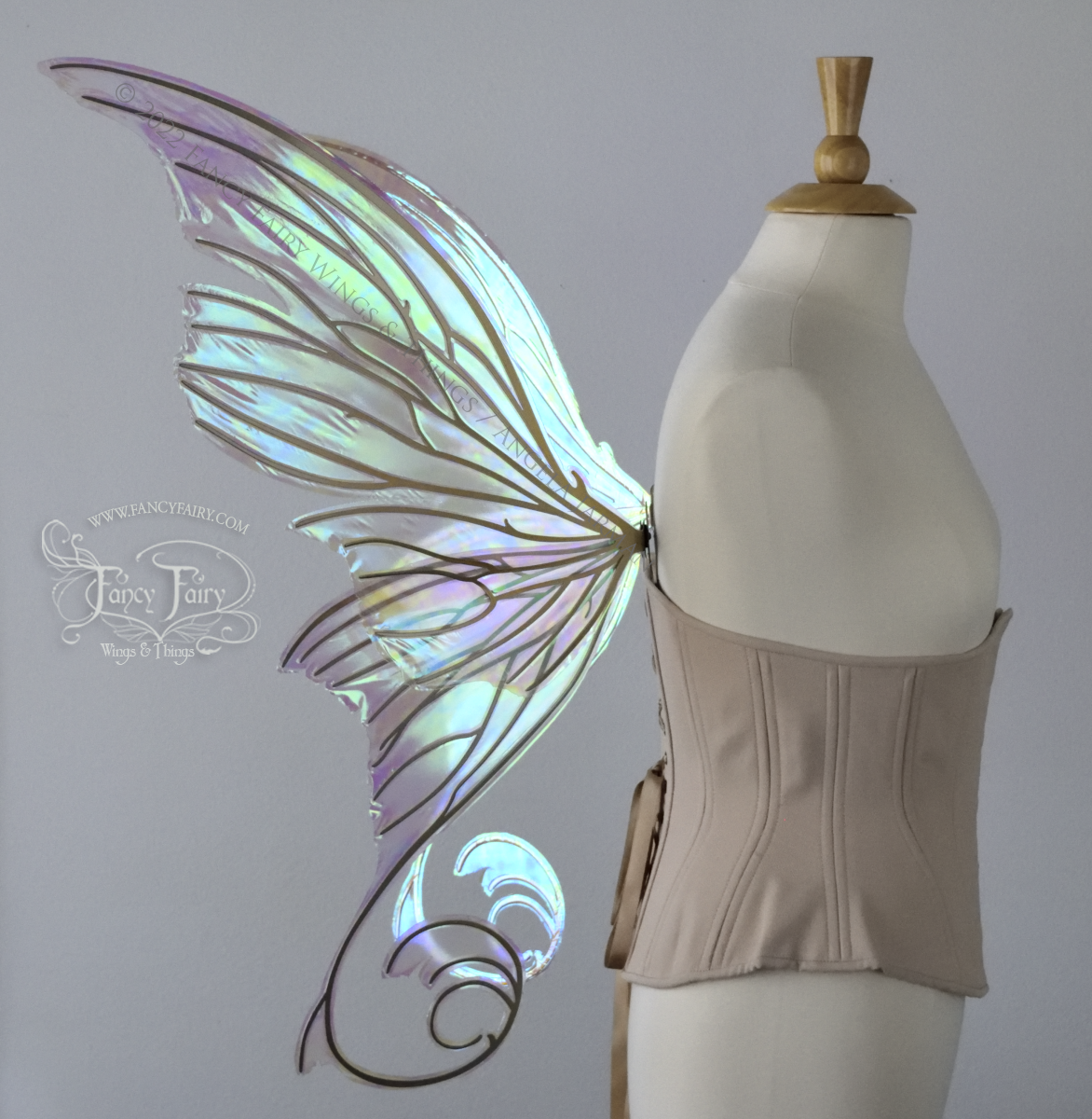 Left side view of a dress form wearing an underbust corset & large green iridescent fairy wings with lots of intricate gold veins, some have 'thorns'. Upper panels curve slightly downwards along top edge with pointy tips, bottom panels have tails