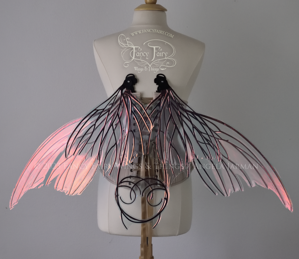 Back view of an ivory dress form wearing an alabaster underbust corset and large pink / orange iridescent fairy wings with lots of intricate black veins, some have 'thorns'. Upper panels curve slightly downwards along top edge with pointy tips, bottom panels have tails, in resting position