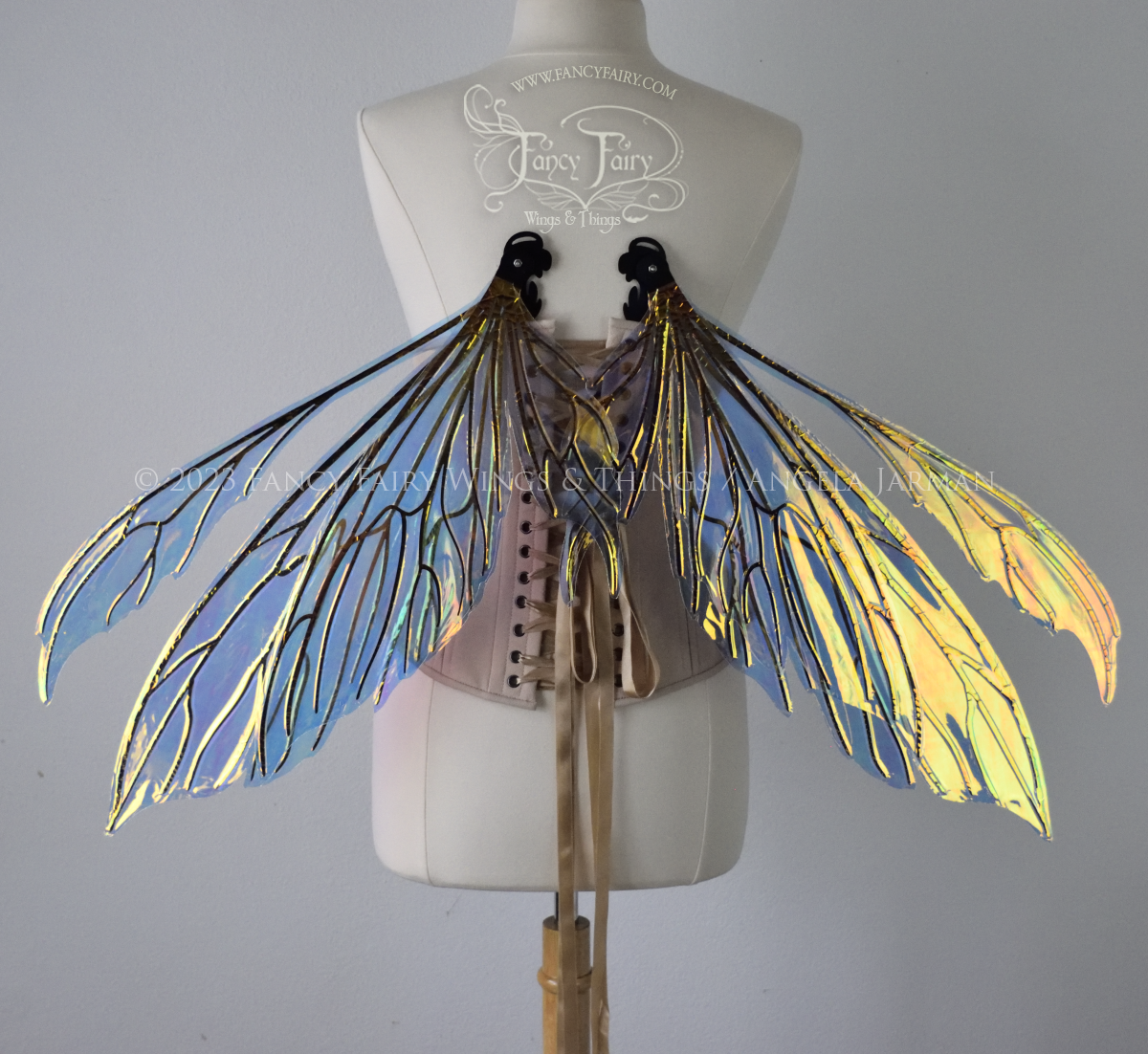 Transparent iridescent fairy wings with 3 panels on each side and antennae with black veins, worn on a dress form, back view in resting position